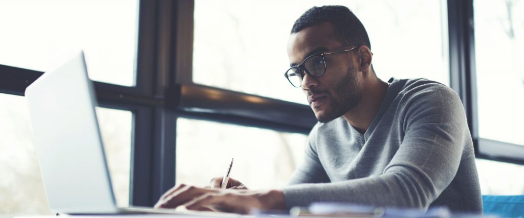 A man taking down notes from an online class